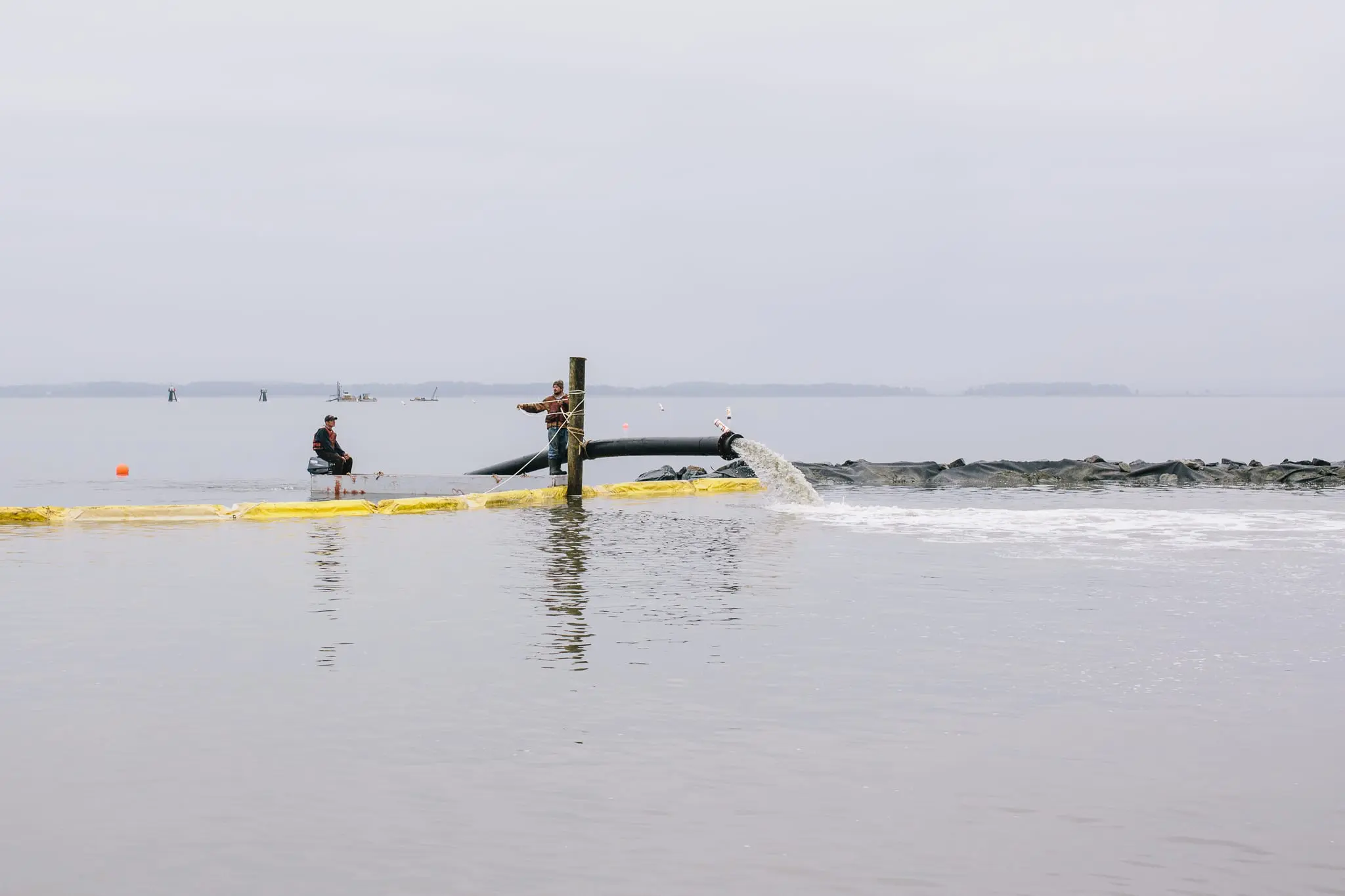 Workers pump sand to construct a living shoreline.